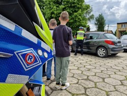 dzieci wraz policjantem stoją w pobliżu radiowozu