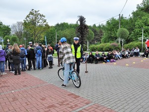 Zdjęcie przedstawia osobę, która porusza się na rowerze, a obok niej stoi policjant, który sprawdza, czy wykonuje ona dobrze zadania.