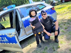 Na zdjęciu widać policjanta z dzieckiem ubranym w hełm oraz kamizelkę kuloodporną