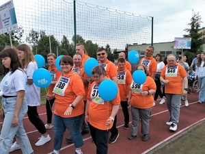 Na zdjęciu widać uśmiechnięte osoby niepełnosprawne w pomarańczowych koszulkach oraz z niebieskimi balonami
