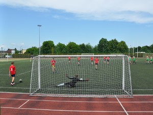 Zdjęcie przedstawia boisko, na którym widać młodzież grającą w piłkę nożną